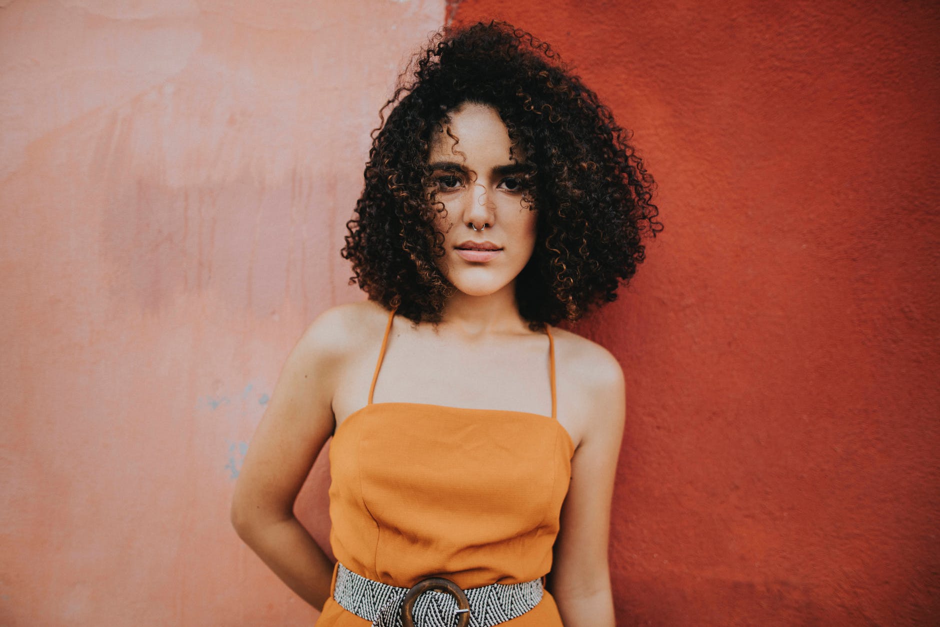 woman wearing an orange top standing beside pink wall