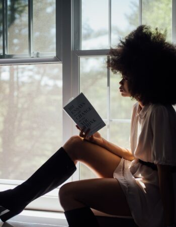 woman sitting on window reading book