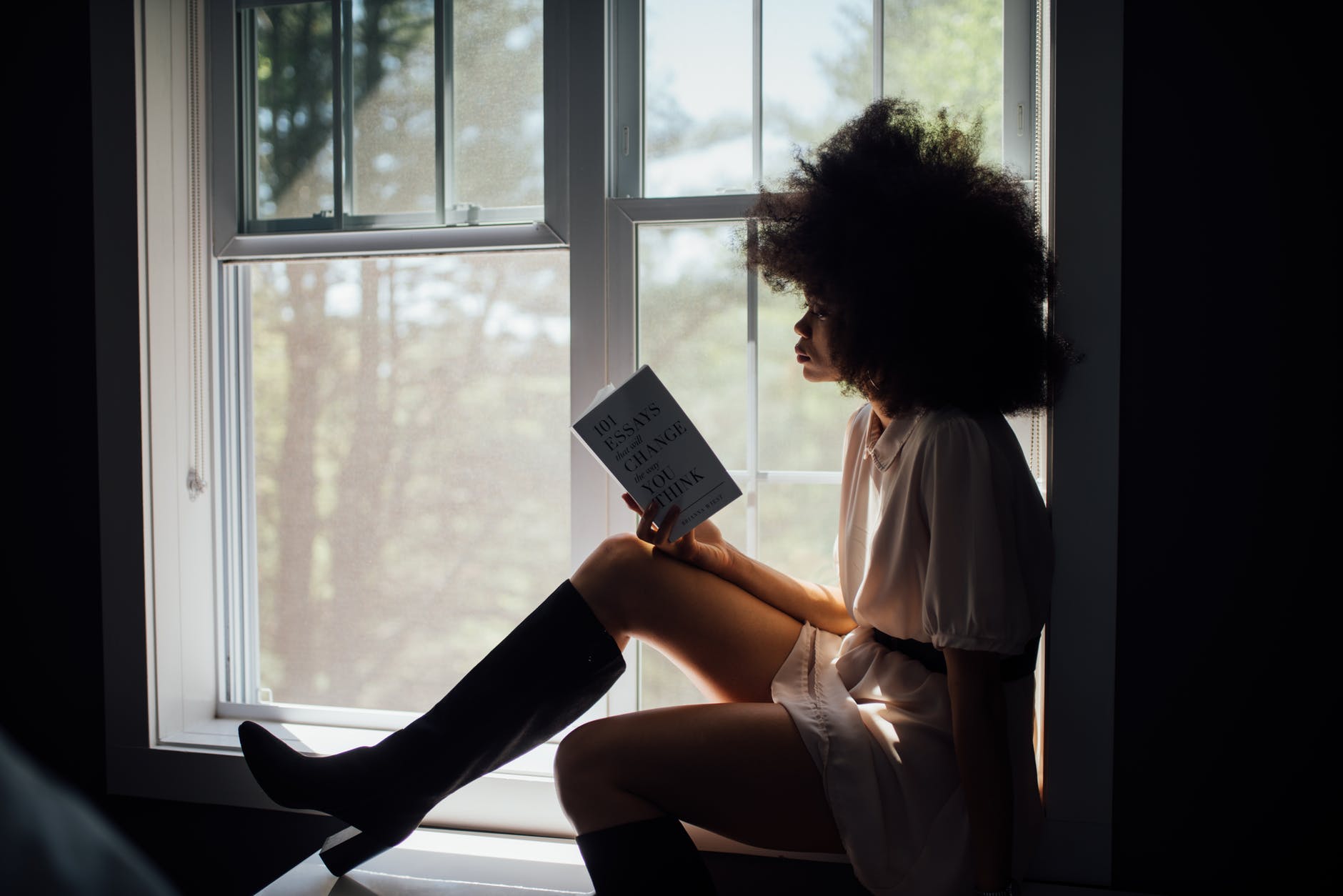 woman sitting on window reading book