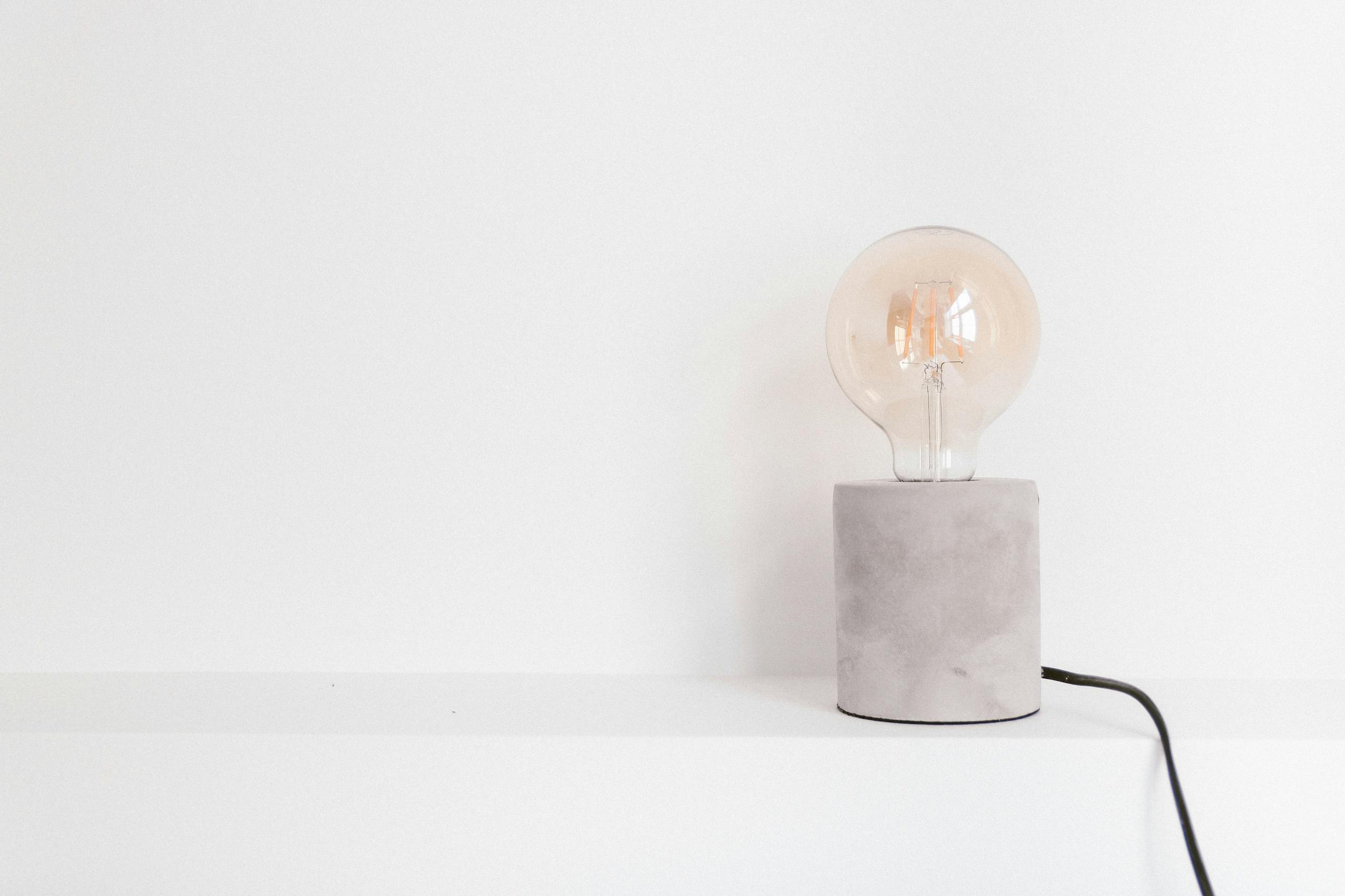 Close-up of an incandescent light bulb on a modern concrete base against a white background.