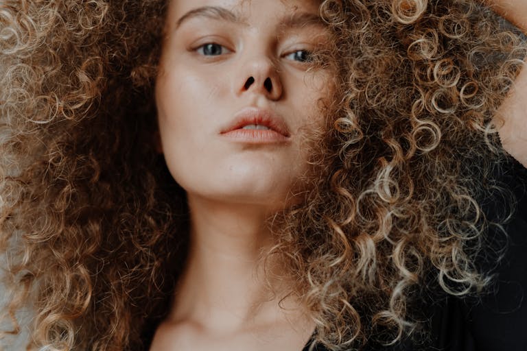 Close-up portrait of a young woman with natural curly hair and minimal makeup.