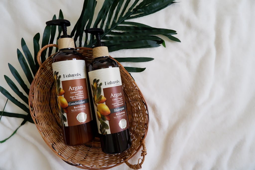 Flat lay of argan oil shampoo and conditioner in a basket with green leaves, perfect for haircare routines.